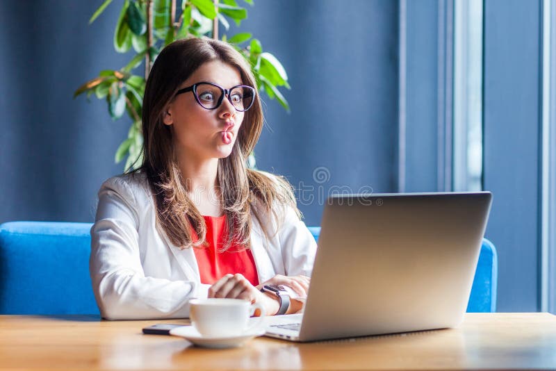 Portrait of funny crazy beautiful brunette young woman in glasses sitting , looking at her laptop display with fish lips and big royalty free stock photos