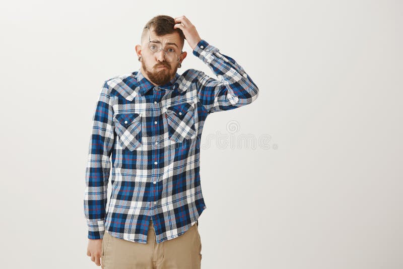 Portrait of funny handsome slim guy with beard, wearing trendy outfit and glasses, scratching head and pouting while stock images Portrait of funny handsome slim guy with beard, wearing trendy outfit and glasses, scratching head and pouting while stock images