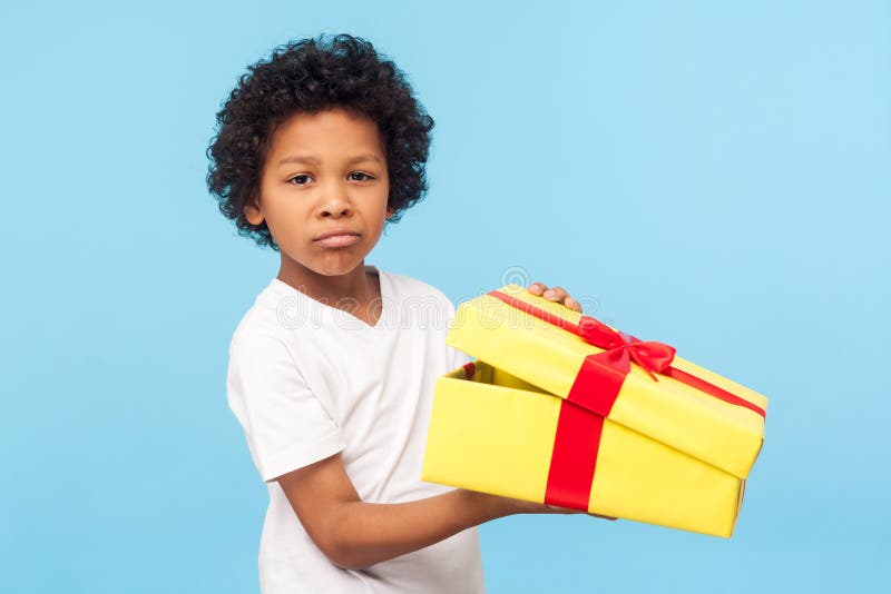 Portrait of funny little boy holding unpacked gift box and looking at camera with upset dissatisfied grimace, naughty capricious child displeased with bad present. indoor studio shot blue background
