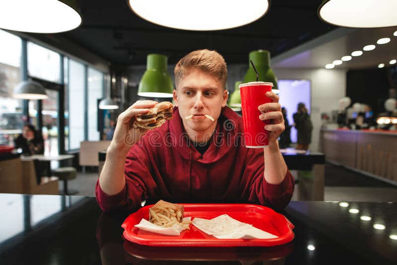 Portrait of a funny young man eating fast food at the background of the restaurant stock image Portrait of a funny young man eating fast food at the background of the restaurant stock image