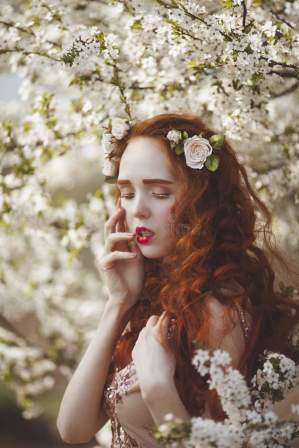 Portrait of A gentle woman with long red hair in a blooming spring garden. Red-haired sensual girl with pale skin and stock photo Portrait of A gentle woman with long red hair in a blooming spring garden. Red-haired sensual girl with pale skin and stock photo