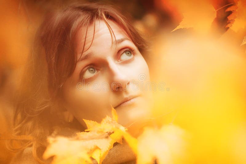 Portrait of a girl close-up through the autumn foliage. A woman`s face in a halo of yellow leaves. Copy space