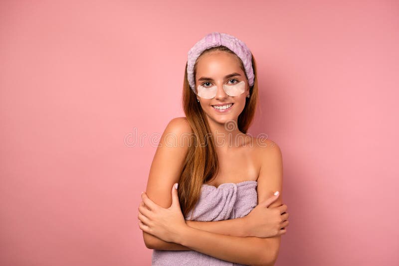 Portrait of a girl with her hair in a towel and patches under her eyes, hugging herself with hands on a pink background. stock images Portrait of a girl with her hair in a towel and patches under her eyes, hugging herself with hands on a pink background. stock images