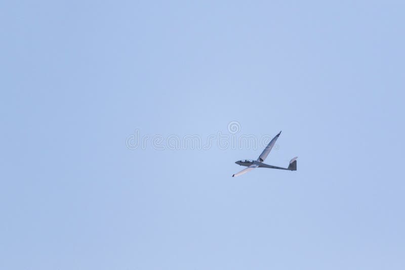 A Portrait of a Glider Plane Flying in the Distance in a Light Blue Sky