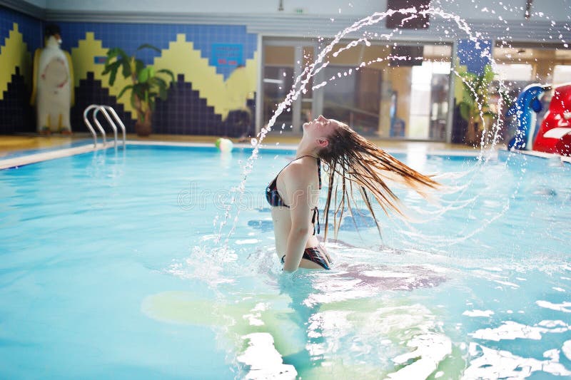 Portrait of a gorgeous firl in bikini making a splash with her hair in the pool in water park