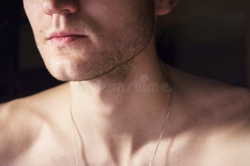 Portrait of a handsome guy with a naked torso. Photo of a close-up in a dark room and light from a lamp. Soft light. Green-eyed br