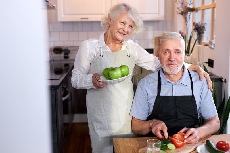 portrait of handsome senior man carving vegetables and wife holding plate with apples royalty free stock photo