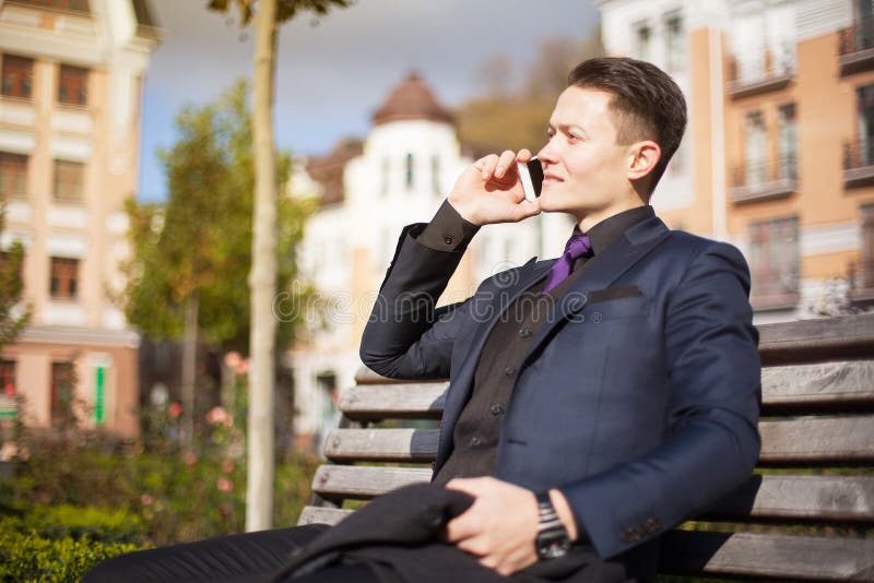 Portrait of a handsome young man with a mobile phone in the park on a bench. Conducts a conversation at lunchtime royalty free stock photo Portrait of a handsome young man with a mobile phone in the park on a bench. Conducts a conversation at lunchtime royalty free stock photo