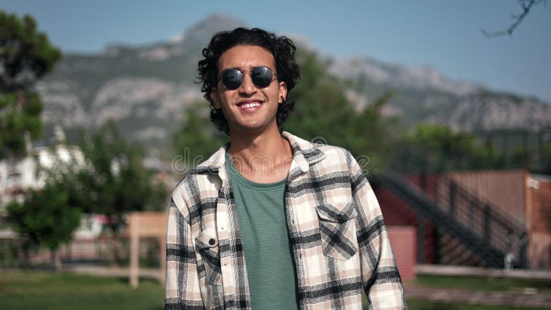 Portrait happy Arabic guy with curly hair posing at summer sunny mountain city park relaxing outdoor stock footage