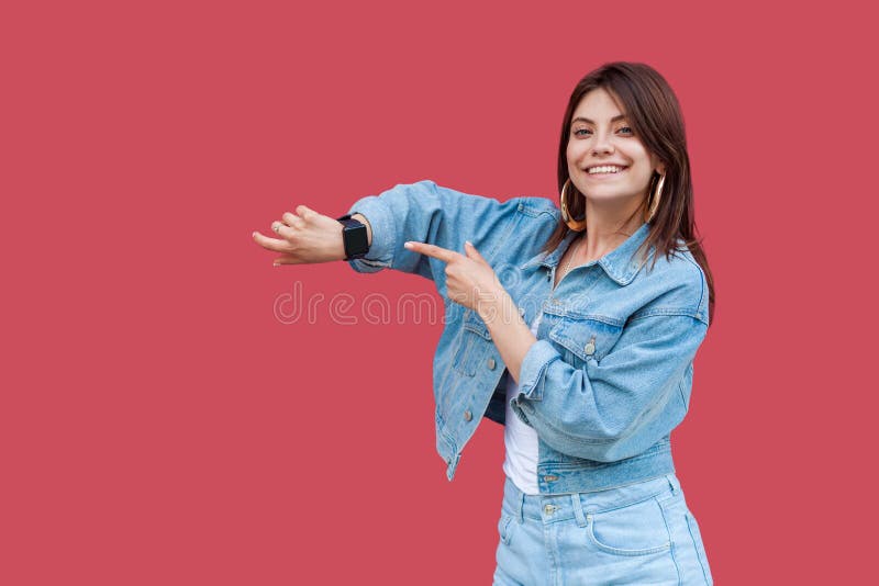 Portrait of happy beautiful brunette young woman with makeup in denim casual style standing showing and pointing at her smart royalty free stock photography