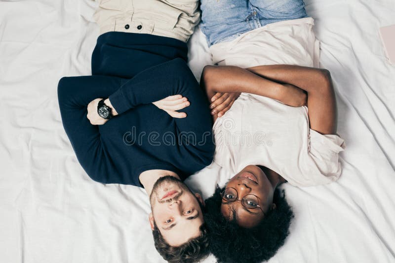 Mixed race couple of young european guy and african girl lying together in bed, relaxing together in their first vacation day, top view. Mixed race couple of young european guy and african girl lying together in bed, relaxing together in their first vacation day, top view.