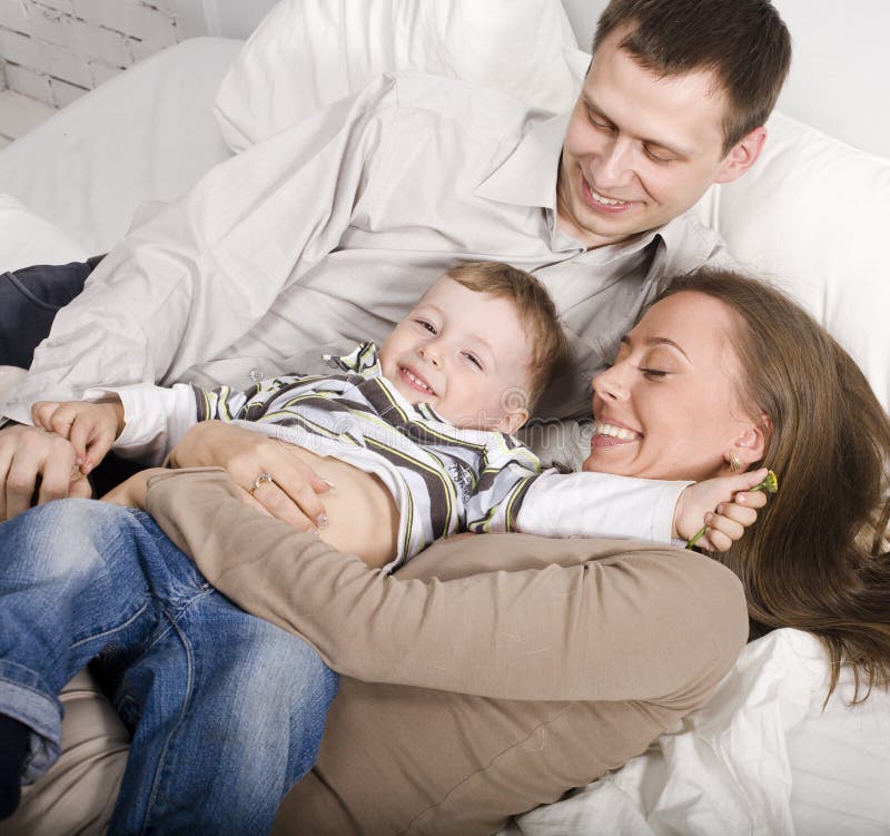 Portrait of happy family, mom and dad playing with their son in bed close up
