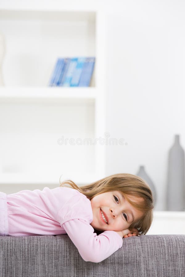 Happy little girl in pink dress, lying on couch, smiling. Lovely european female stock images, royalty-free photos and pictures