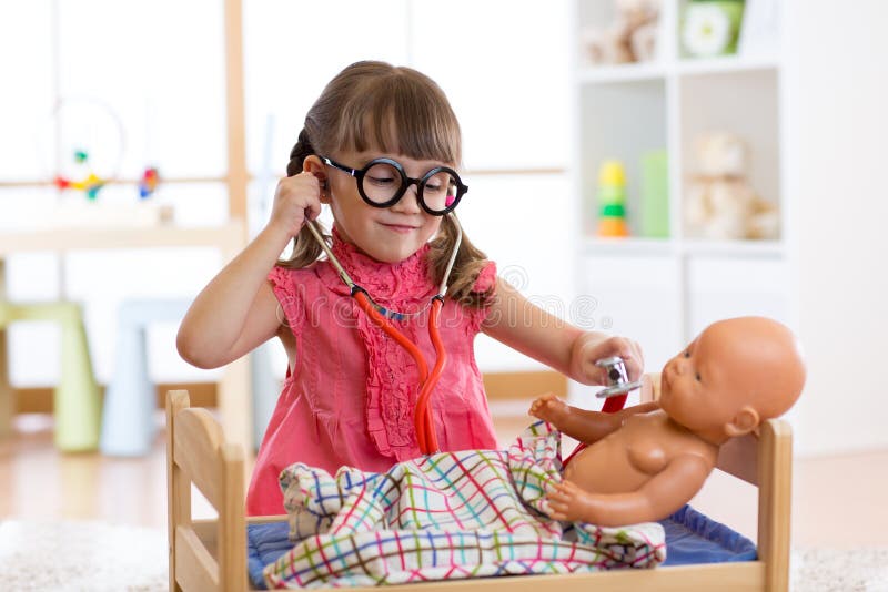 Portrait of happy girl 3 years old with glasses at home or nursery room with doll, playing doctor