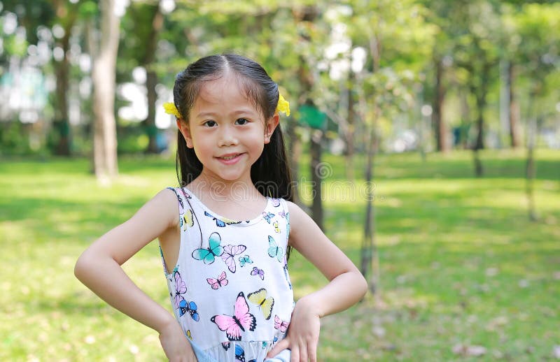 Portrait of happy little Asian child girl with yellow flower on ears in summer garden outdoor