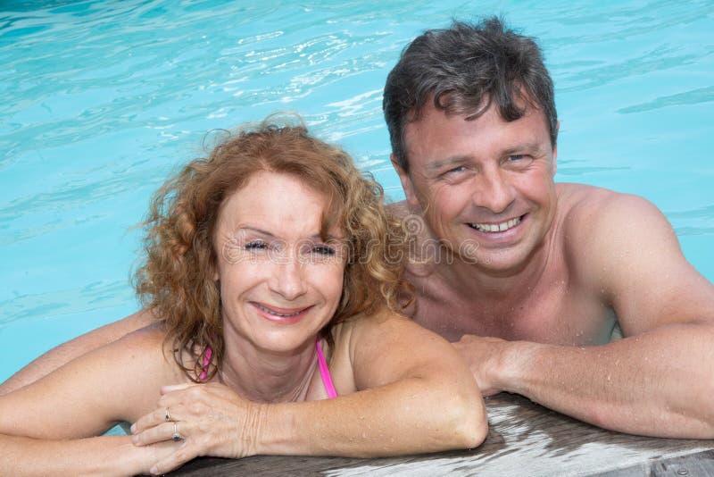 Portrait of happy middle aged couple relaxing on the edge of swimming pool