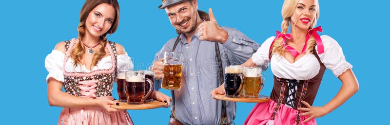 Portrait of happy Oktoberfest man and two women, wearing a traditional Bavarian clothes, serving big beer mugs on blue stock photos Portrait of happy Oktoberfest man and two women, wearing a traditional Bavarian clothes, serving big beer mugs on blue stock photos