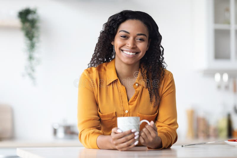 Cheerful young Black woman in loungewear drinking cup of morning coffee in  her kitchen and laughing at funny memes on smartphone screen Stock Photo -  Alamy