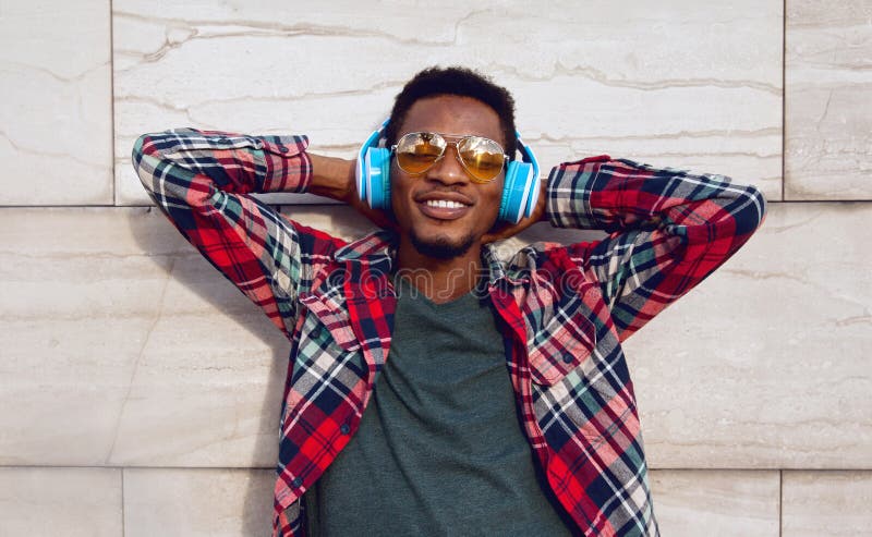 Portrait happy smiling african man with wireless headphones enjoying listening to music in city on gray wall background