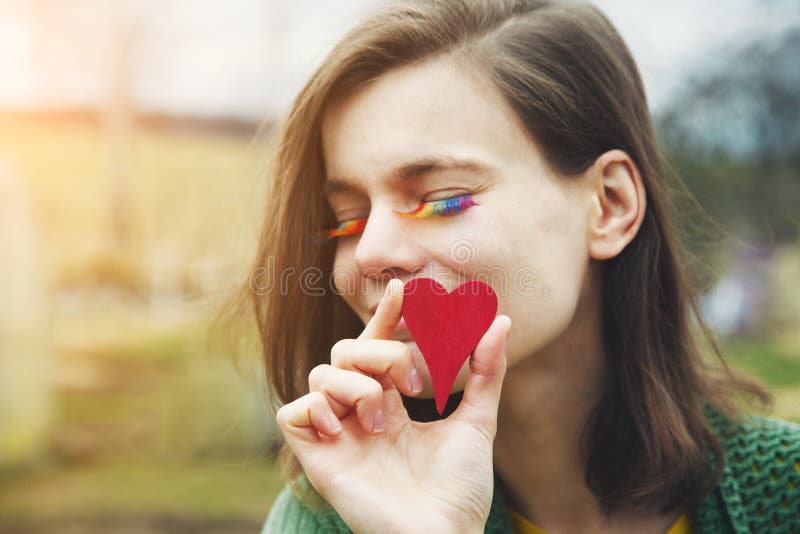 Portrait of happy smiling beautiful young woman with rainbow lgbtq eyelashes holding red wooden heart next to her face royalty free stock images Portrait of happy smiling beautiful young woman with rainbow lgbtq eyelashes holding red wooden heart next to her face royalty free stock images