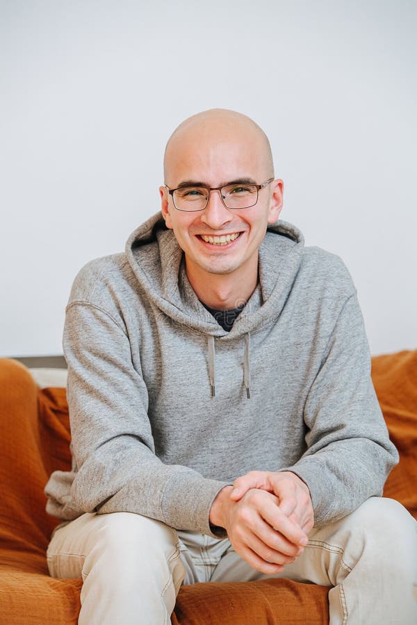 Portrait of a happy smiling happy bold man in glasses sitting on a sofa