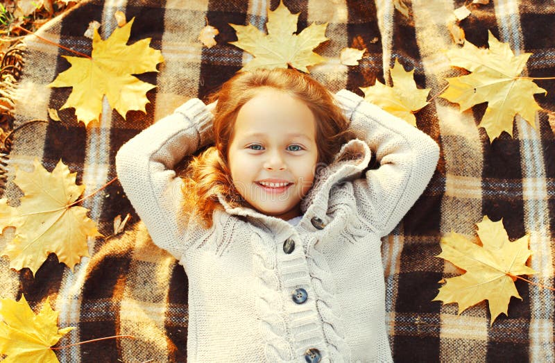 Portrait happy smiling child lying having fun with yellow maple leafs in autumn day top view