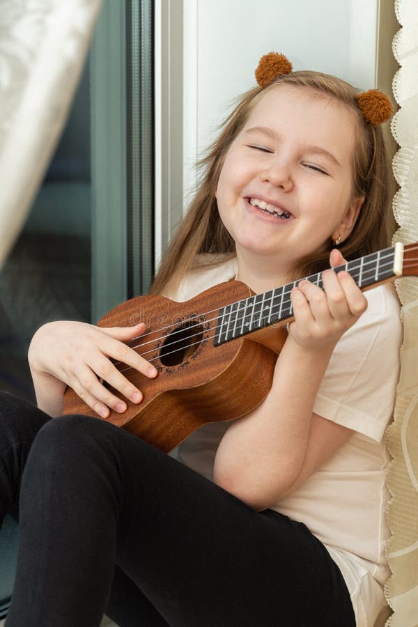 Cute little girl in summer clothing playing ukulele over pink