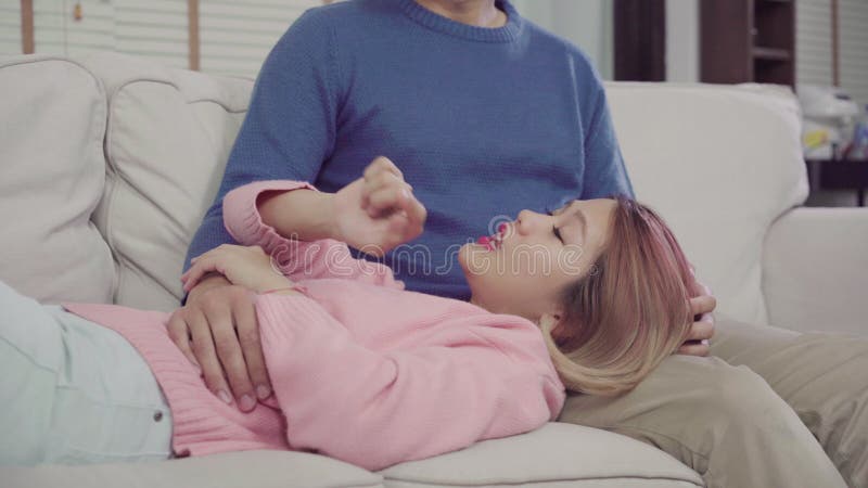 Portrait of happy sweet Asian couple have romantic time lying on the sofa when relax in their living room at home.