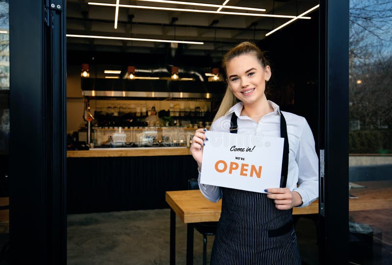 Waitress at restaurant entrance showing open sign to customers.