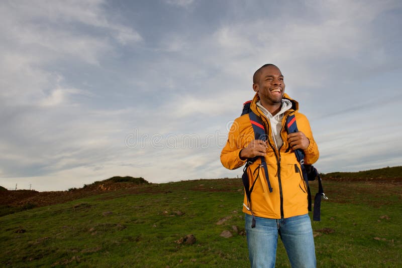 Portrait of happy young black man backpacking through fields