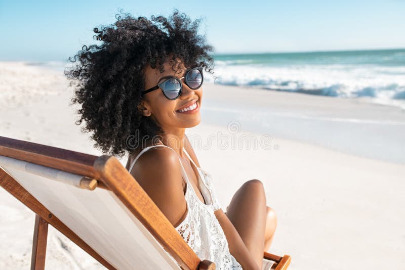 Happy smiling african woman sitting on deck chair at beach