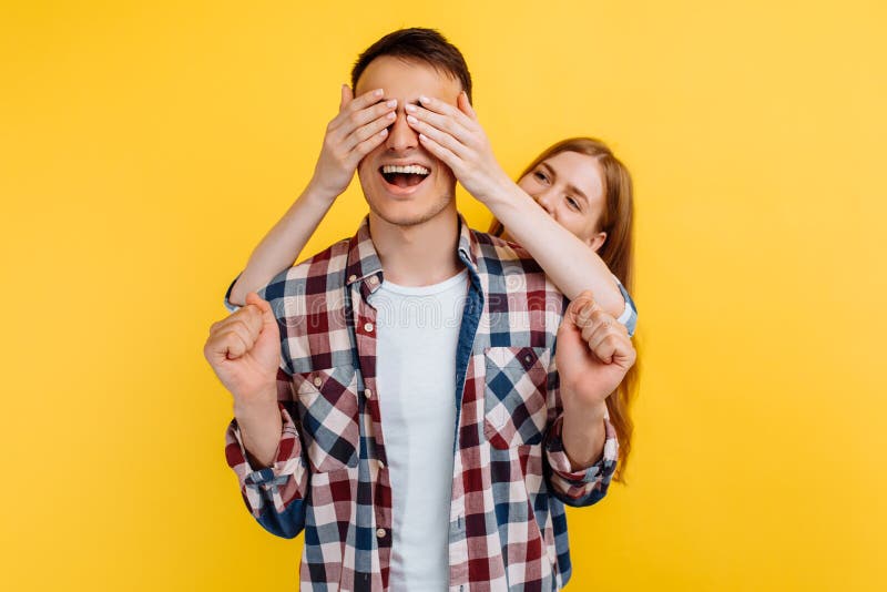 Portrait of a happy young couple, beautiful woman makes a surprise, closes the eyes of a man, on a white background, Valentine`s