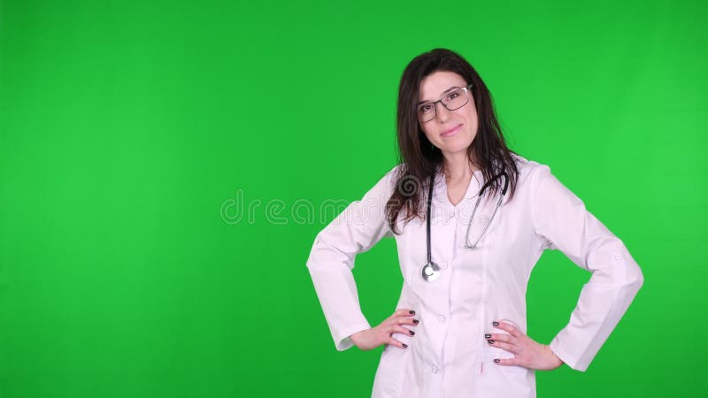 Portrait of happy young female doctor in glasses, dressed in white medical uniform and with stethoscope, presenting