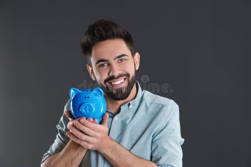 Portrait of happy young man with piggy bank on grey background