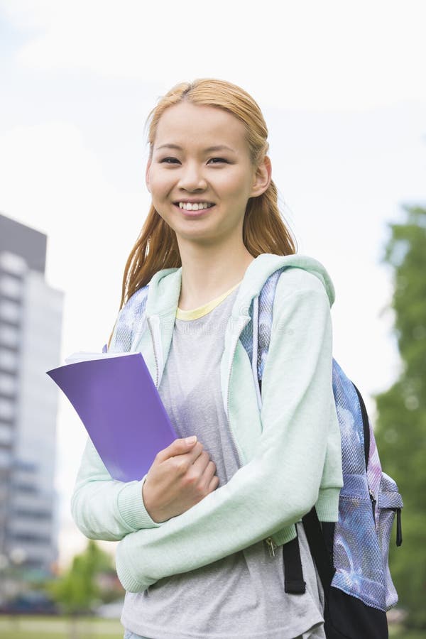 Portrait of Happy Young Woman Holding Book at College Campus Stock