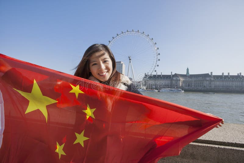 Portrait of happy young woman holding Chinese flag against London Eye at London, England, UK