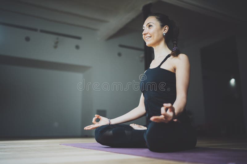 Portrait of happy young woman practicing yoga indoor. Beautiful girl practice lotus position in class.Calmness and relax