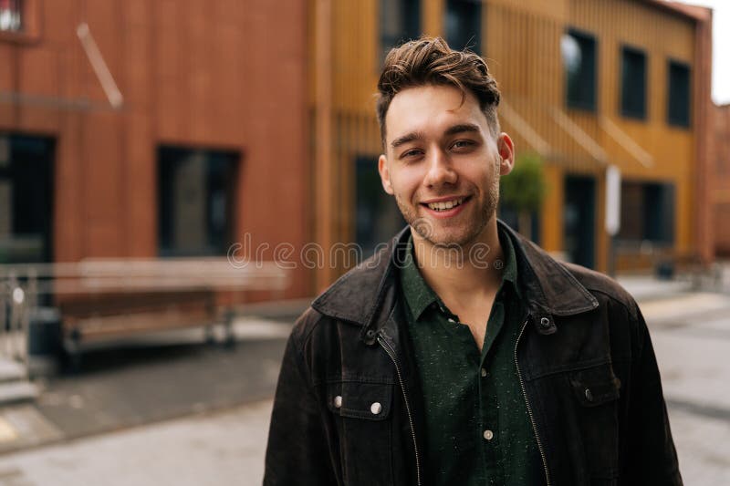 Portrait haut de la taille du beau jeune homme barbu portant une veste noire et une chemise verte souriant en regardant la caméra photo stock