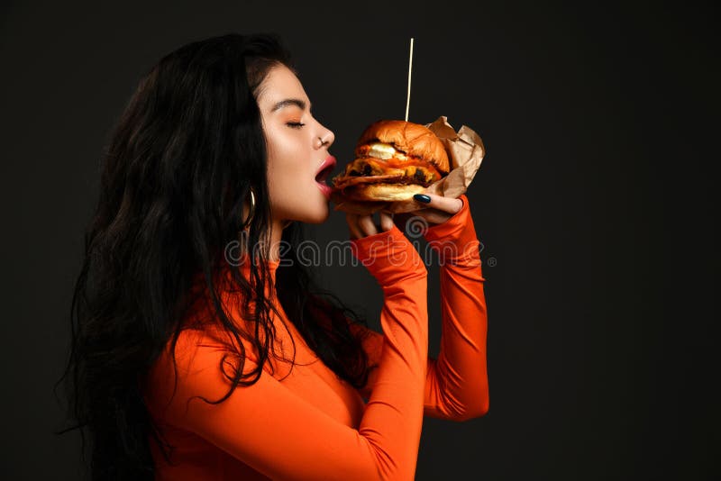 Portrait of hot sexy brunette woman with pouty lips in tight red clothes eating biting fresh big tasty craft burger