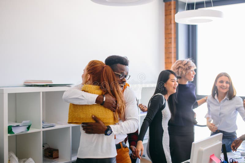 Portrait of hugging African and Caucasian partners showing their close relationship in modern office building