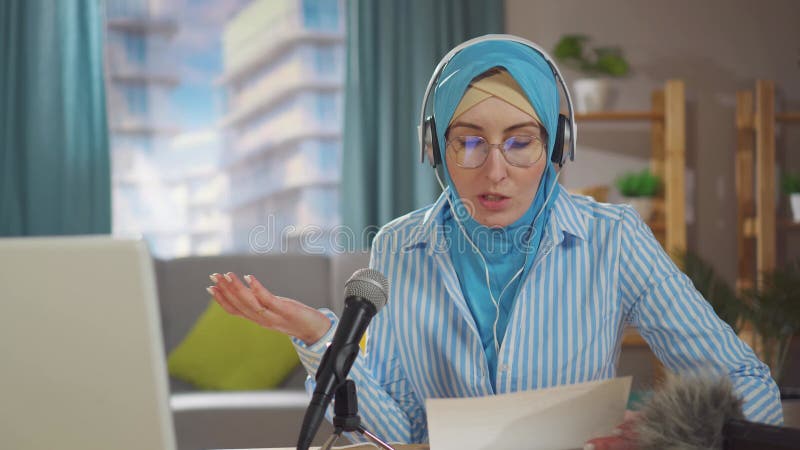 Portrait jeune femme musulmane enregistre un podcast assis devant un micro dans son salon clips vidéos