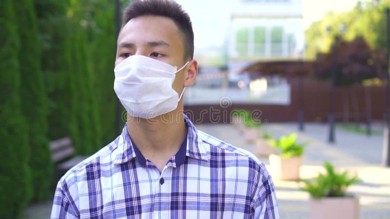 Portrait jeune homme asiatique portant un masque mÃ©dical dans la rue dans le parc ralenti