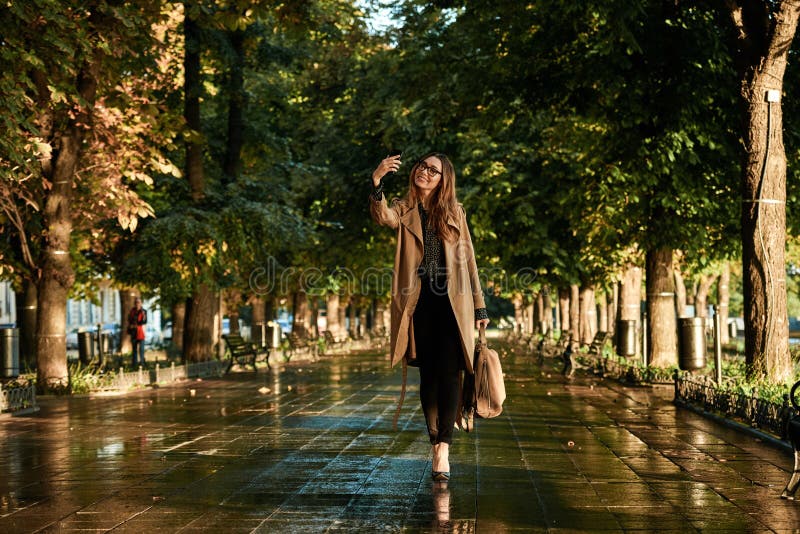 Portrait of joyous woman using cell phone while walking through empty alley. Portrait of joyous woman 20s wearing coat and eyeglasses using cell phone while royalty free stock photos Portrait of joyous woman using cell phone while walking through empty alley. Portrait of joyous woman 20s wearing coat and eyeglasses using cell phone while royalty free stock photos