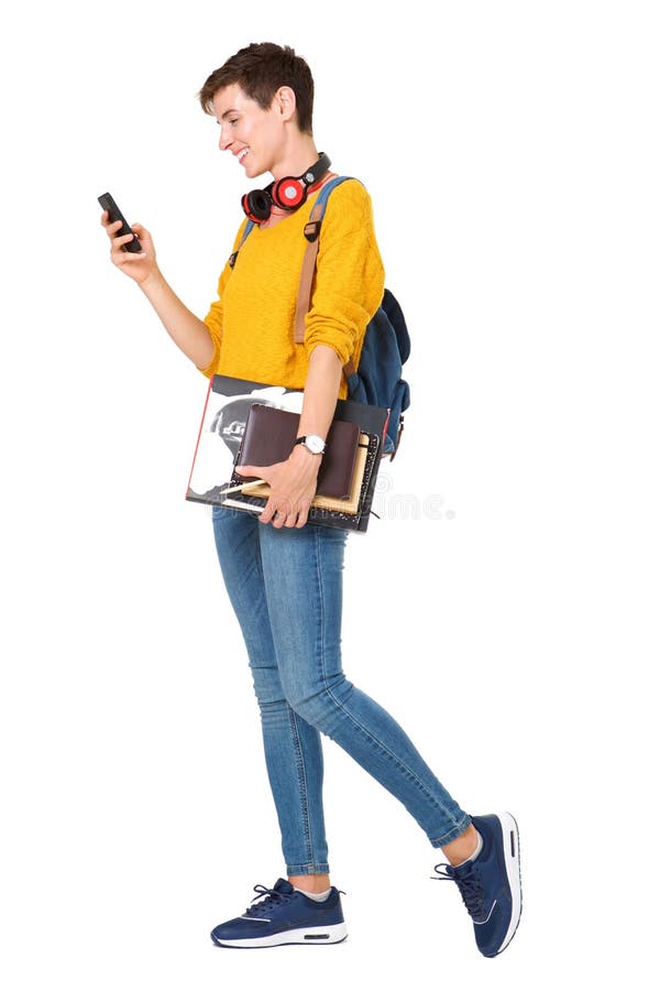 Portrait latéral de jeune femme heureuse marchant avec le sac, livres et regardant le téléphone portable photos libres de droits Portrait latéral de jeune femme heureuse marchant avec le sac, livres et regardant le téléphone portable photos libres de droits