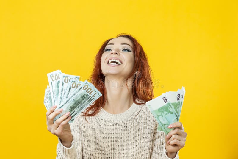 Portrait of Laughing Cheerful Young Winsome Woman Holding Stack of Money Banknotes and Celebrating Isolated over Yellow Background