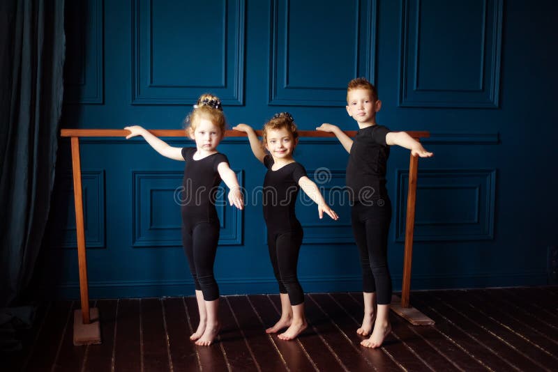 Portrait of 3 little children two girls ballerina and small boy dancer in black leotard practicing at ballet barre at dance studio