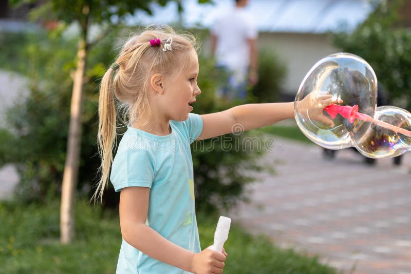 Portrait of little cute caucasian blond girl having fun and joy blowing big soap bubbles playing on city street park outdoors. stock photos Portrait of little cute caucasian blond girl having fun and joy blowing big soap bubbles playing on city street park outdoors. stock photos