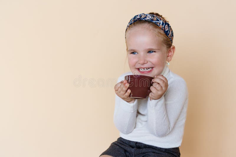 Portrait of a little cute girl sitting and smiling, holding cup of hot drink cocoa enjoying, over beige background. stock photography Portrait of a little cute girl sitting and smiling, holding cup of hot drink cocoa enjoying, over beige background. stock photography