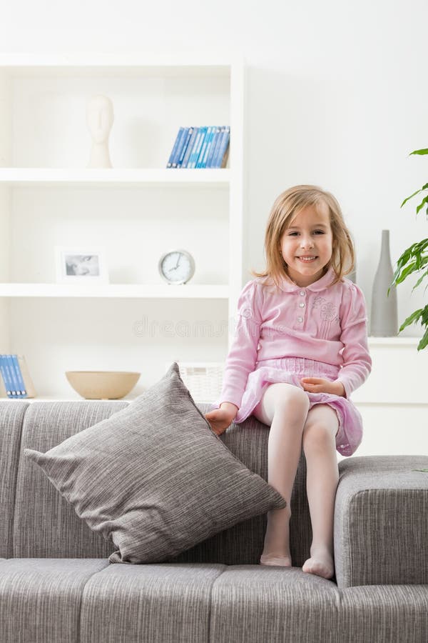 Portrait of happy little girl in pink dress, sitting on couch, smiling. Lovely european female stock images, royalty-free photos and pictures