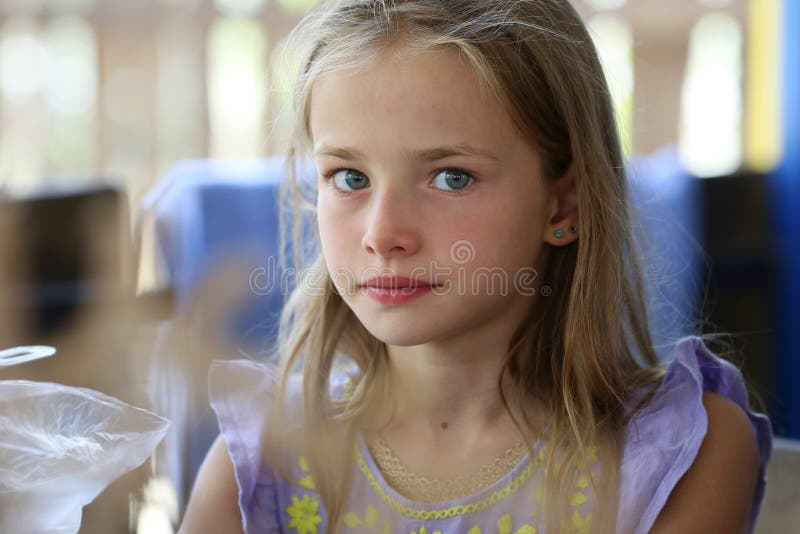 Portrait of a little girl with long hair and blue eyes of a blonde who is resting in nature, is seriously